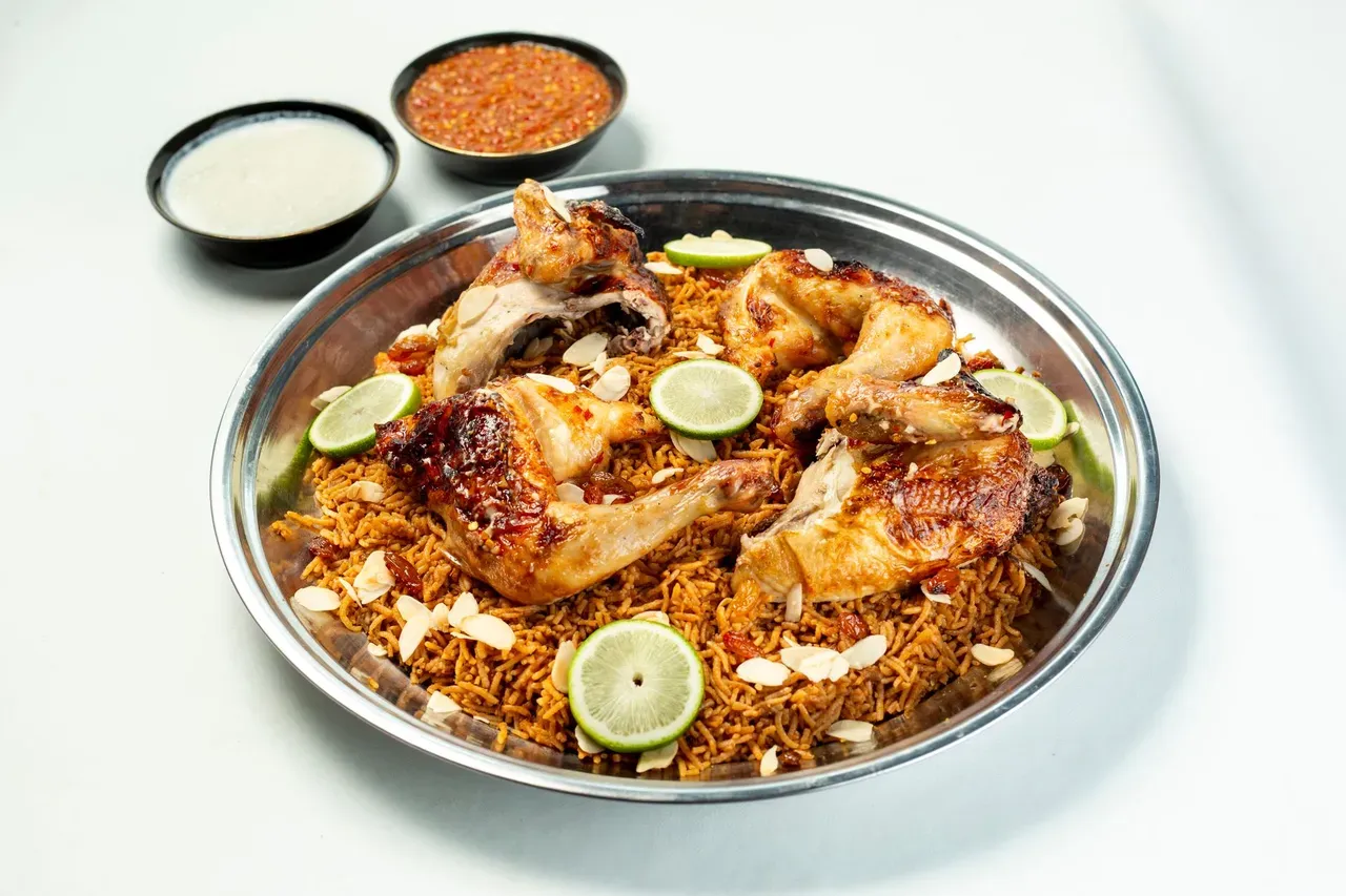 Briani mauricien au poulet servi sur un plateau avec citron et herbes fraîches, le plat en couches.